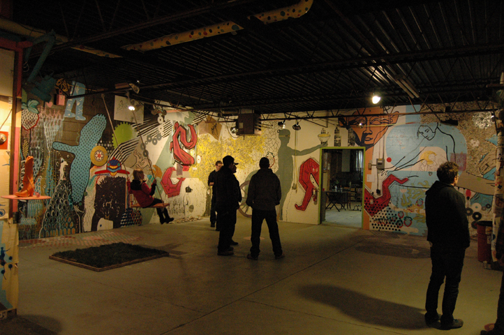 People in an art show where the walls are collaged. Dinderbeck Studios.