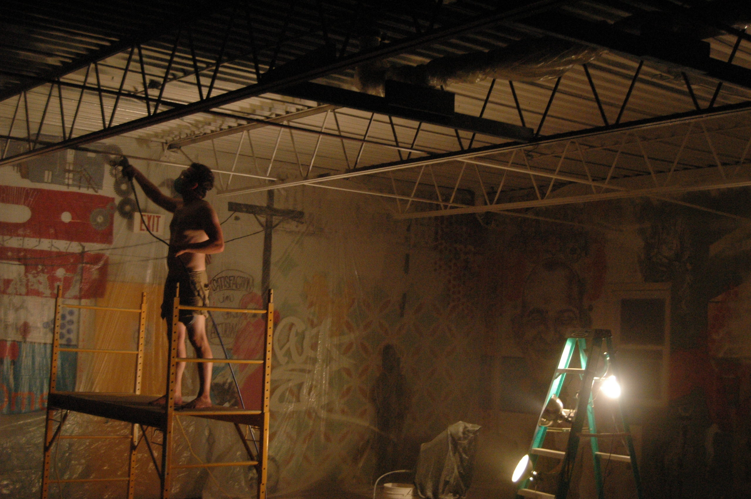 A person painting the ceiling of an open room with collages on the walls. Dinderbeck Studios.