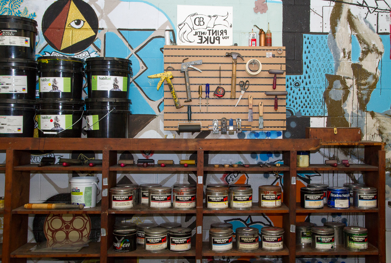 Assorted inks in cans on shelves and tools for printing hanging on a wall